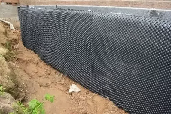 Dimpled drainage board installed against an excavated exterior foundation wall before backfilling