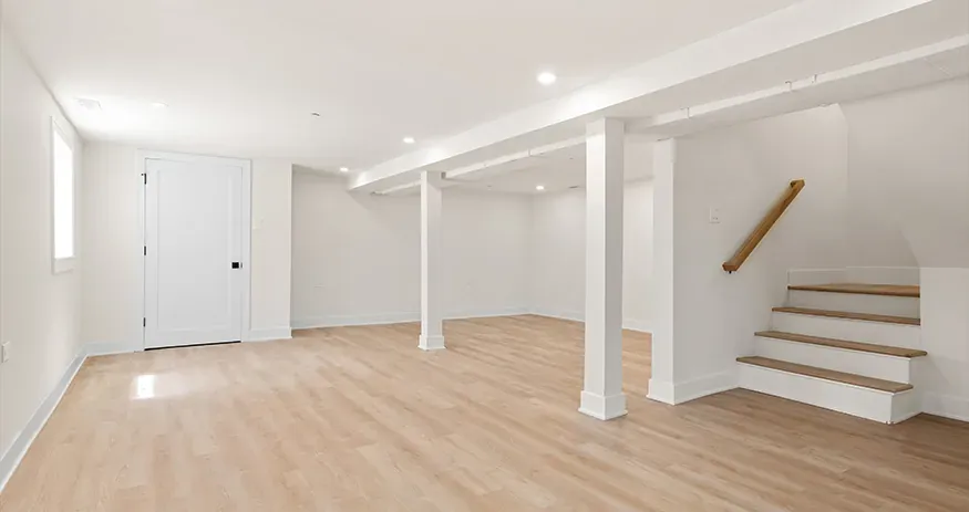 A finished, dry basement living space with light wood flooring and a painted staircase