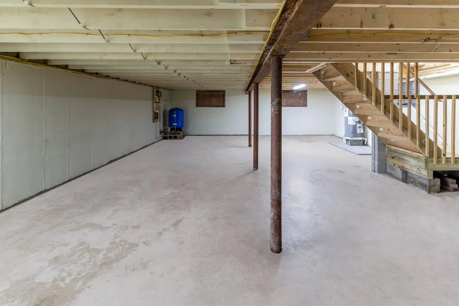 An unfinished basement with a low ceiling, exposed joists and steel support posts