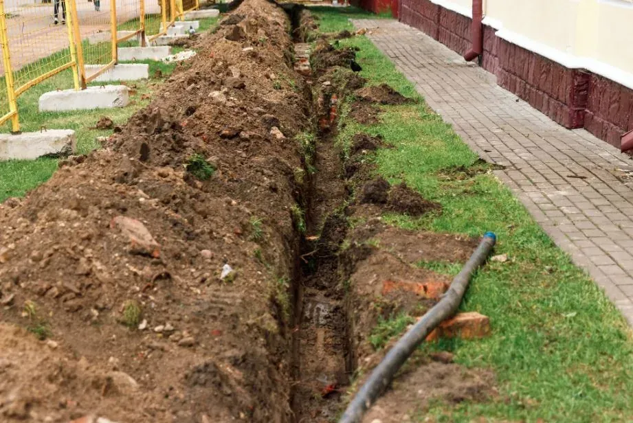 An excavated yard drainage trench running alongside a lawn beside a house